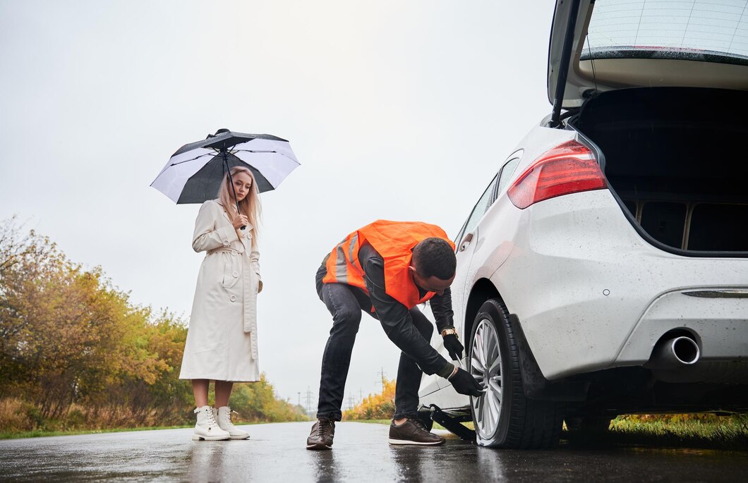 dépannage atra à gaillac, technicien changeant une roue sous la pluie pendant qu’une conductrice attend